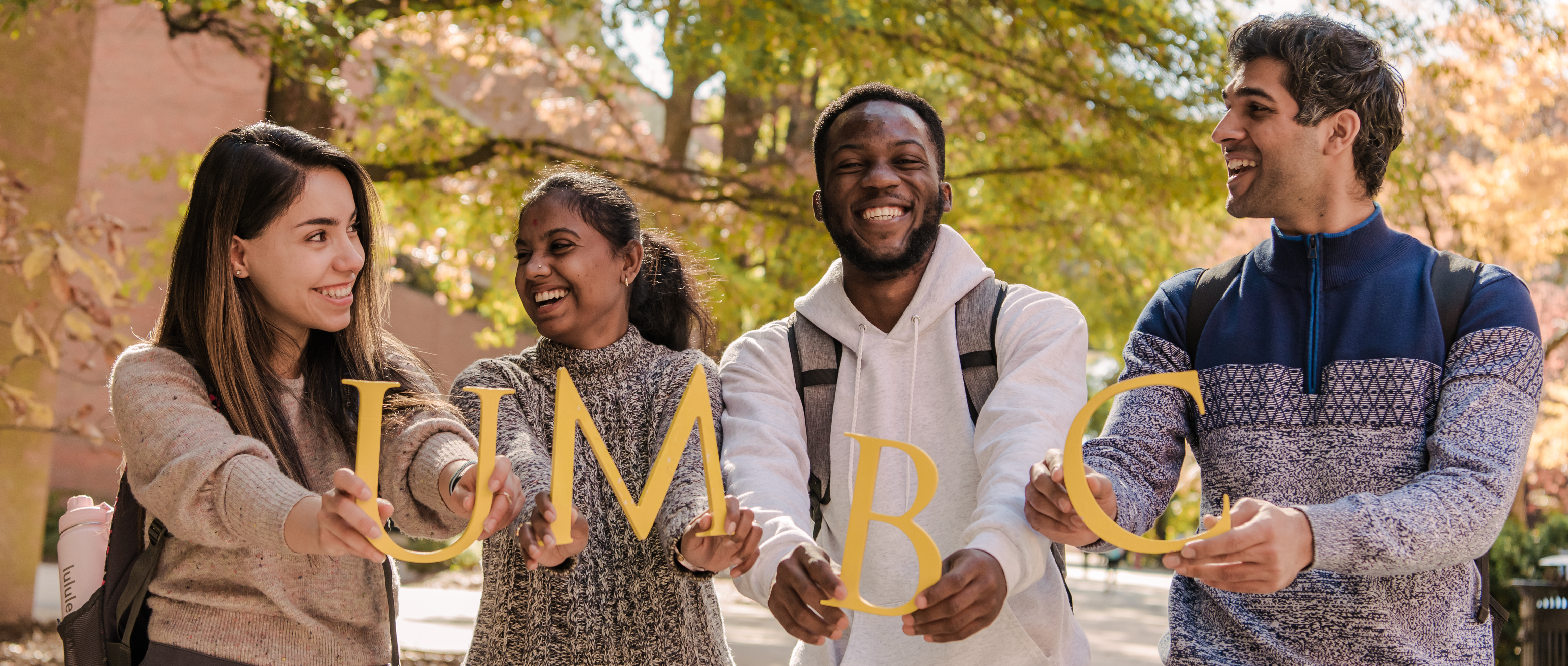 Four students holding gold UMBC letters laughing and smiling