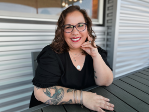 Candace Doan sitting at a table smiling with head resting on hand.